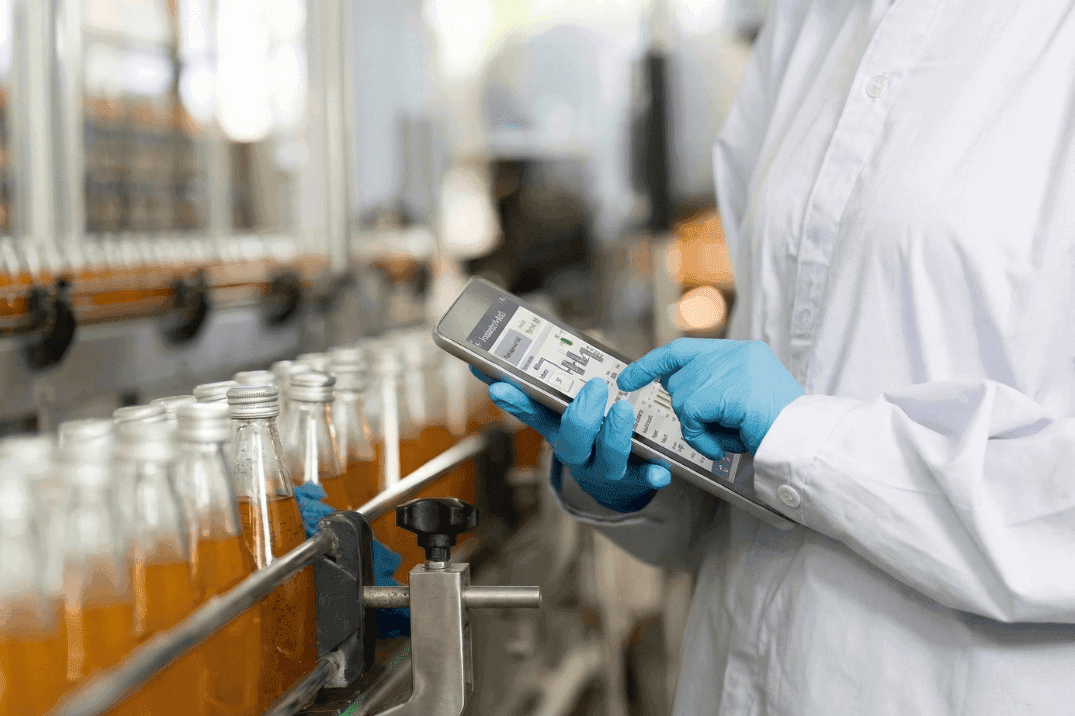 Operator using a handheld device to monitor conveyor system performance on a food and beverage production line, supporting real-time analysis and bottleneck identification
