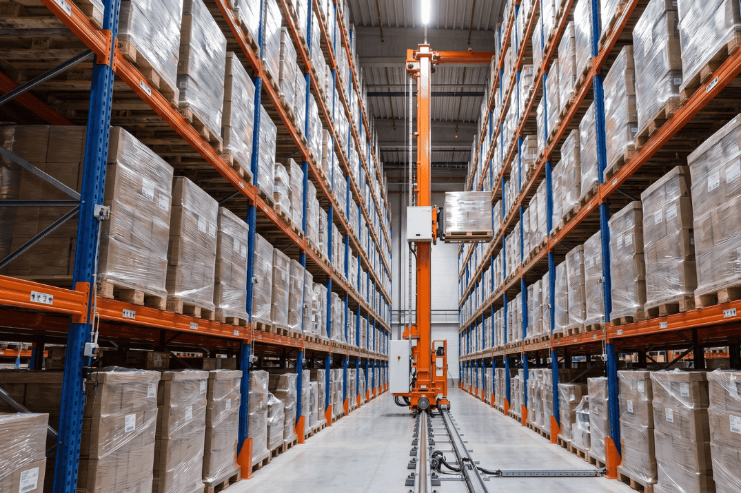 Stacker crane operating within a high-bay automated storage and retrieval system, moving palletised goods along racking aisles in a warehouse environment