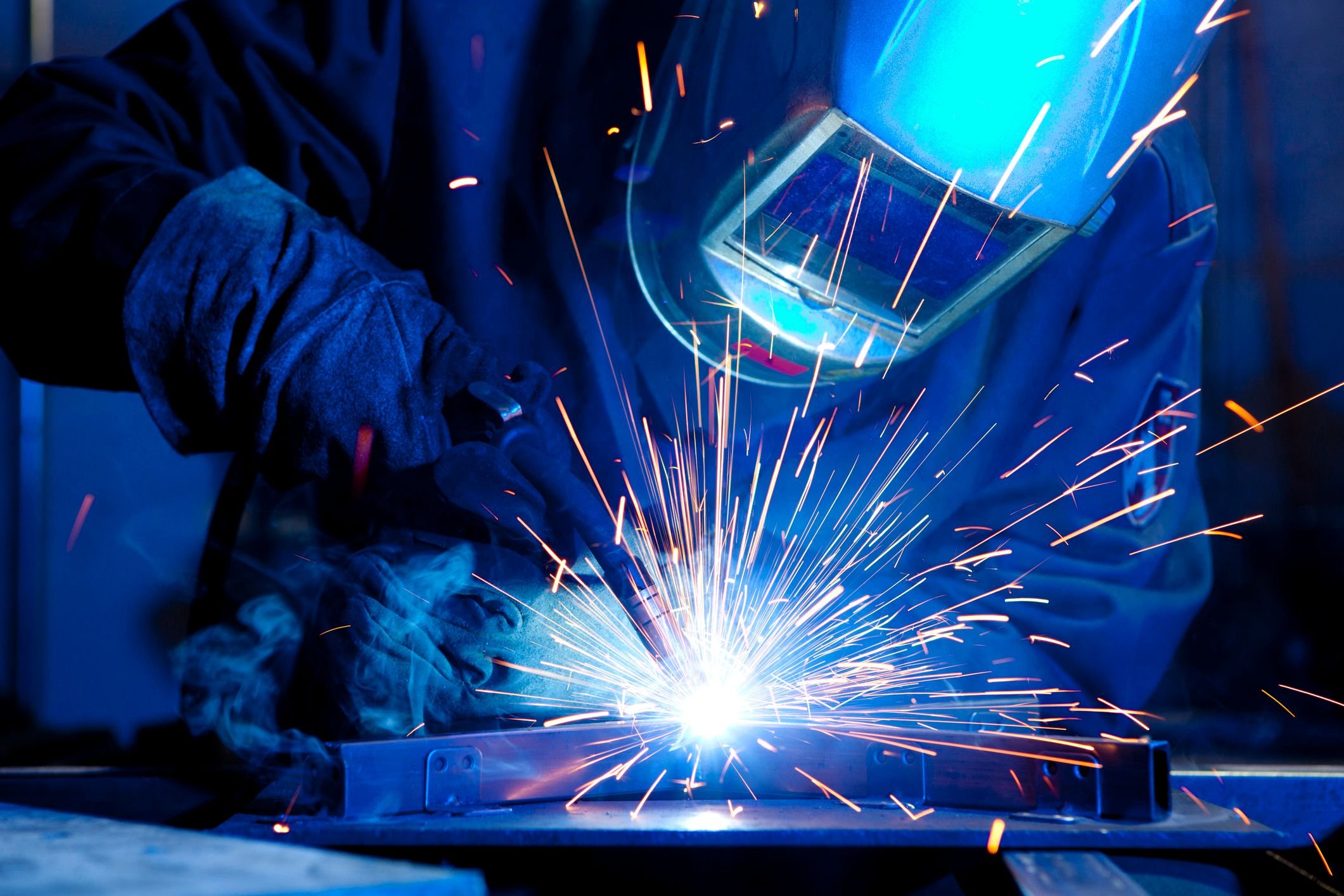 A worker in a welding helmet building a conveyor system, representing the manufacturing industry.